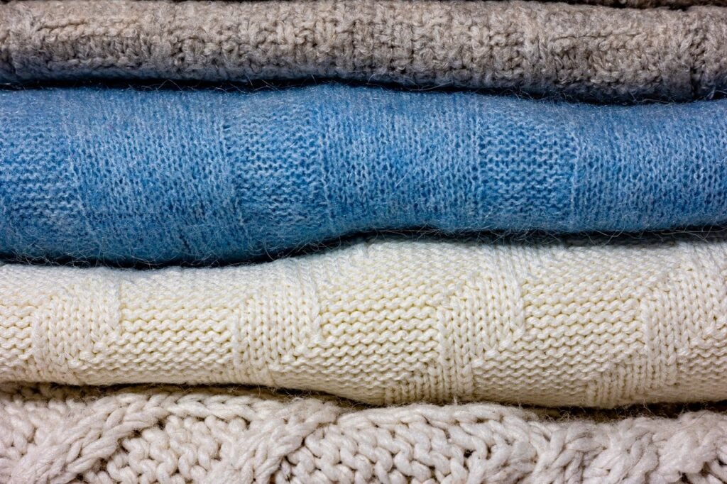 A close-up of various colorful knitted wool fabrics stacked together.