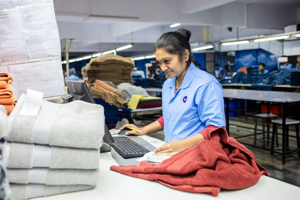 Female factory worker inspecting textiles for quality control in a busy production facility.